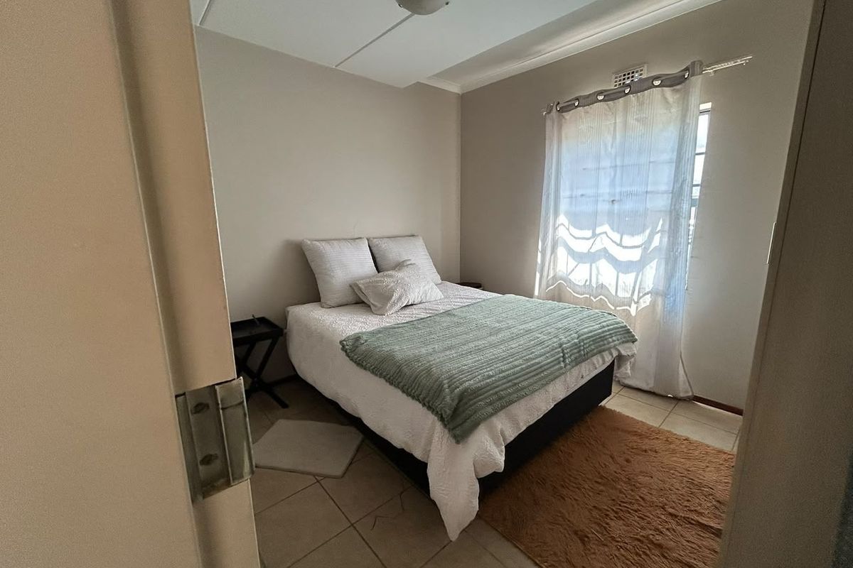 A compact bedroom featuring tiled flooring and a window with natural light, providing a functional and neutral living space.