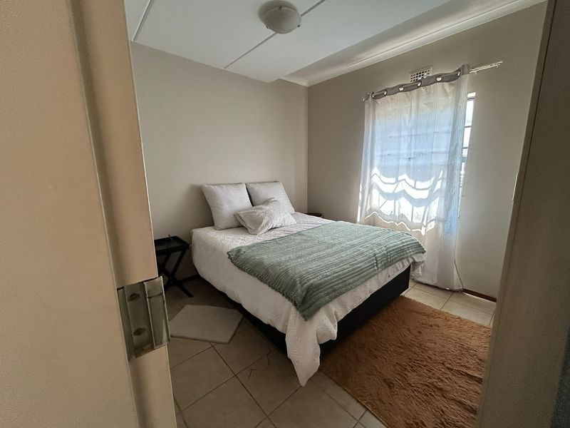 A compact bedroom featuring tiled flooring and a window with natural light, providing a functional and neutral living space.