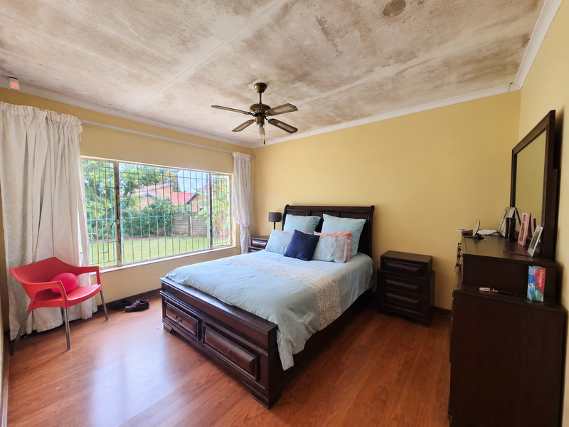 A bedroom featuring laminate flooring, a ceiling fan, and security bars on the window, currently showing significant water damage to the ceiling.