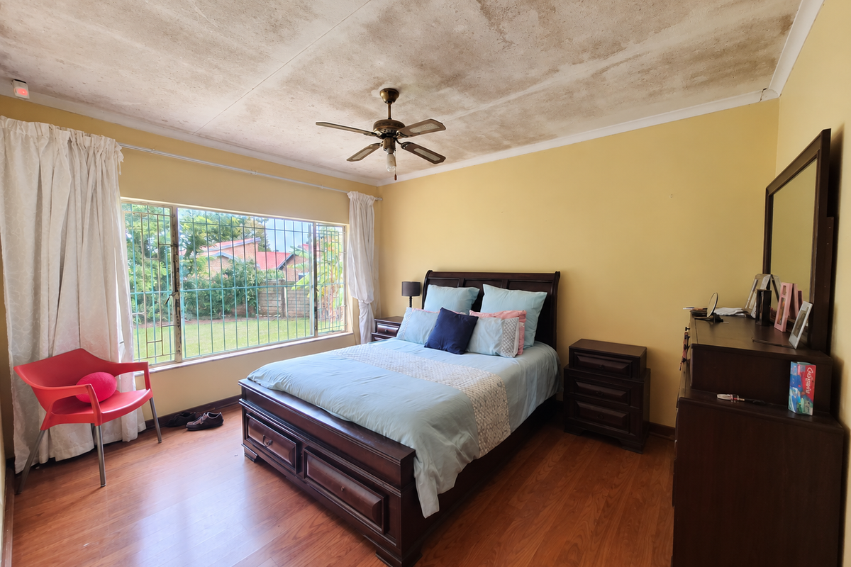 A bedroom featuring laminate flooring, a ceiling fan, and security bars on the window, currently showing significant water damage to the ceiling.