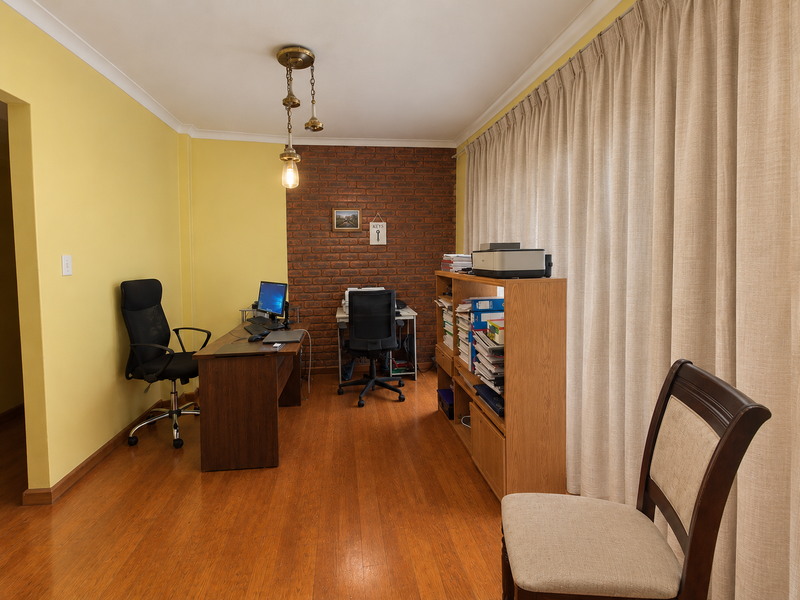 A functional home office featuring an exposed brick accent wall, warm laminate flooring, and large windows dressed with full-length curtains.