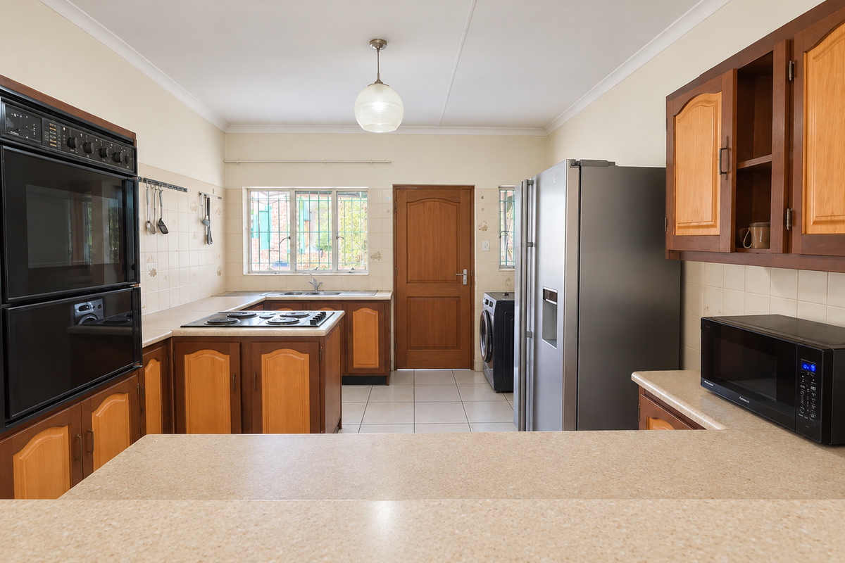 Functional kitchen featuring timber cabinetry, laminate countertops, built-in oven, electric hob, and tiled flooring with direct access to the rear exterior.