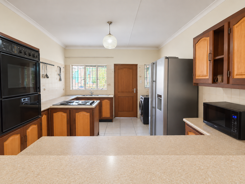 Functional kitchen featuring timber cabinetry, laminate countertops, built-in oven, electric hob, and tiled flooring with direct access to the rear exterior.