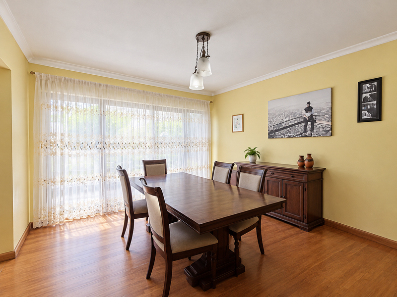 A well-maintained dining room featuring warm laminate flooring, cove cornicing, and a large sliding glass door that provides ample natural light.