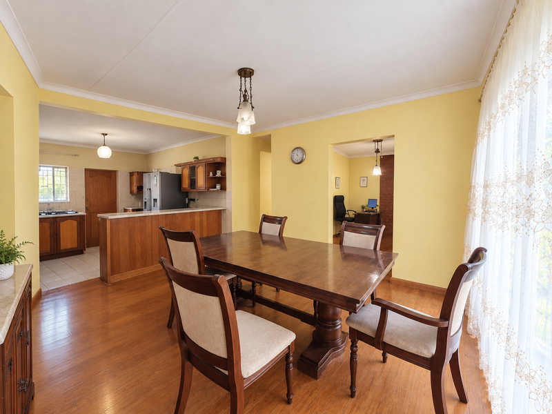 Open plan dining area featuring laminate flooring and coved ceilings, seamlessly connecting to a functional kitchen with built-in cabinetry and a breakfast bar.
