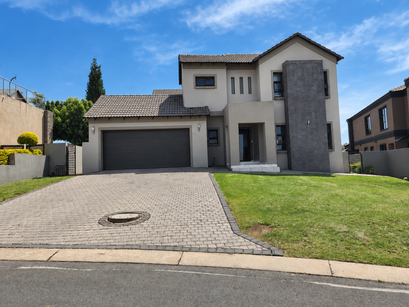 Modern double-story residential home featuring a paved driveway, double garage, and attractive stone-clad architectural detailing set against a well-maintained lawn.