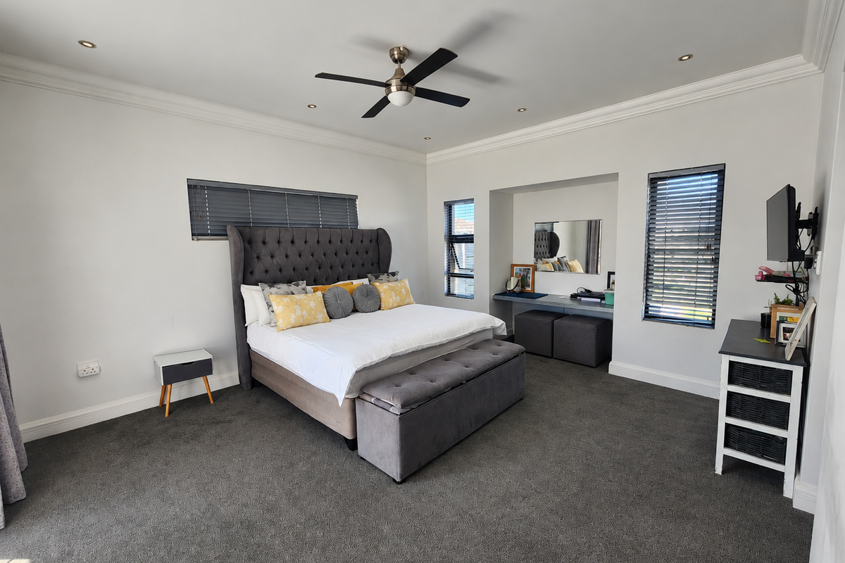 Spacious bedroom featuring neutral walls, plush carpeting, recessed lighting, a ceiling fan, and a built-in vanity area with integrated storage.