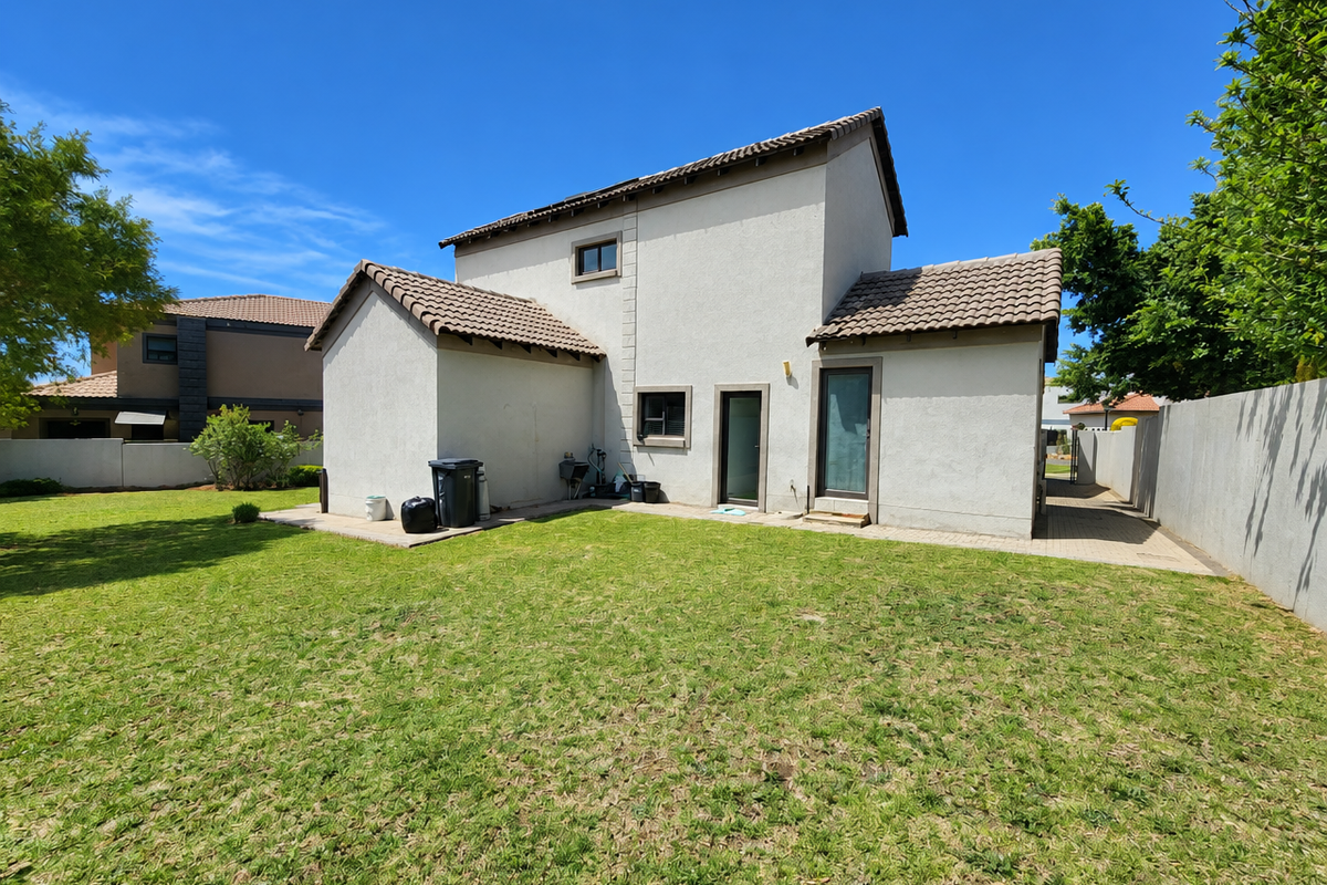 Rear view of the house featuring a tiled roof, plastered exterior walls, a paved patio area, and a well-maintained lawn.