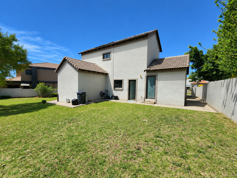 Rear view of the house featuring a tiled roof, plastered exterior walls, a paved patio area, and a well-maintained lawn.