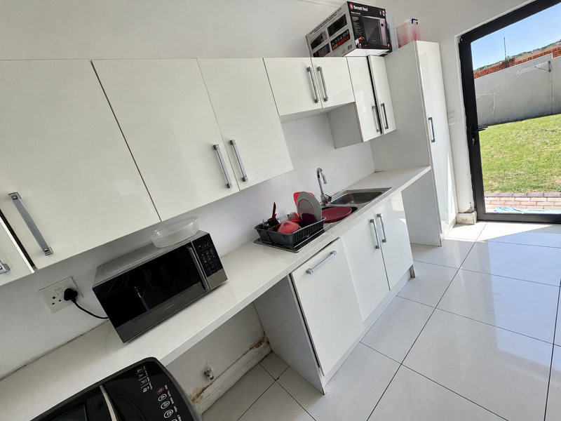 A functional kitchen featuring white cabinetry, tiled flooring, and direct access to the rear garden through a glass sliding door.
