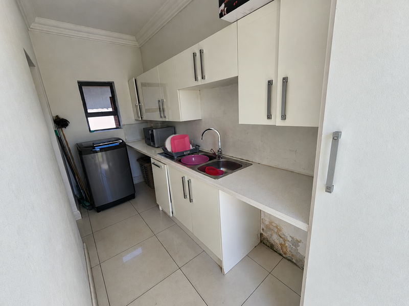 Compact scullery area featuring built-in cabinetry, a stainless steel sink, and tiled flooring, with visible water damage on the lower wall section.