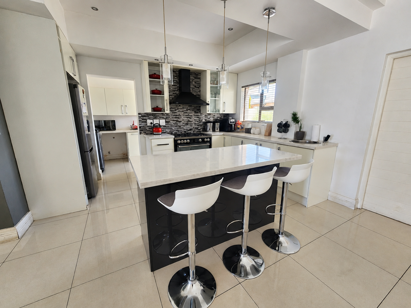 Modern kitchen featuring a central island with stone countertops, gas hob, extractor fan, and sleek cabinetry, complemented by tiled flooring and contemporary pendant lighting.
