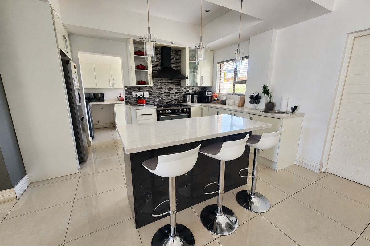 Modern kitchen featuring a central island with stone countertops, gas hob, extractor fan, and sleek cabinetry, complemented by tiled flooring and contemporary pendant lighting.