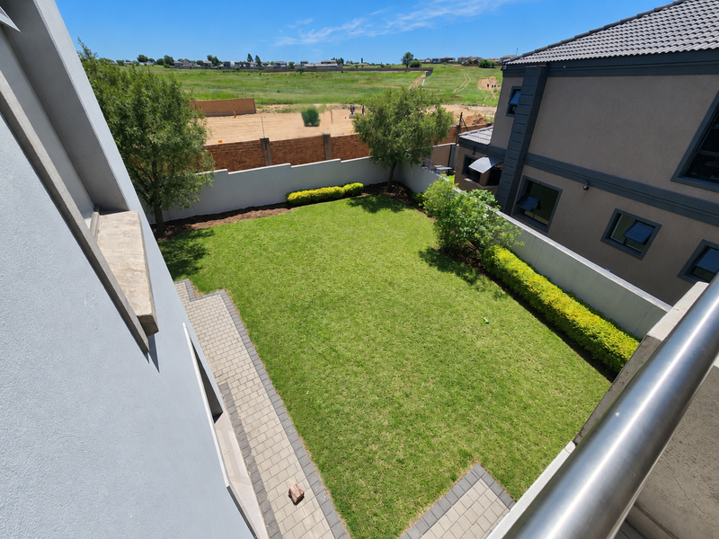 A well-maintained rear garden featuring a manicured lawn, paved pathways, and perimeter boundary walls, viewed from an elevated balcony.