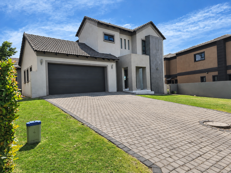Modern double-story residential home featuring a paved driveway, double garage, and contemporary stone-clad architectural detailing.