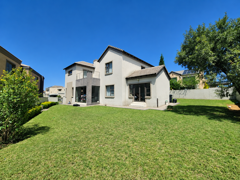 Rear view of the house featuring a spacious lawn, tiled roof, balcony, and sliding door access to the garden.