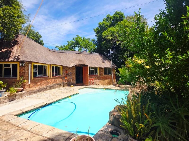 Outdoor pool area featuring a swimming pool with paved decking, set against a brick house with a traditional thatch roof.