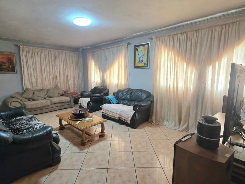 A spacious living room featuring tiled flooring and large windows with curtain treatments, offering a functional and comfortable layout.