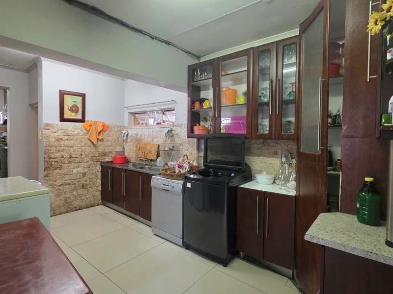 A functional kitchen featuring dark wood cabinetry, stone-cladding backsplash, tiled flooring, and a dedicated pantry area with glass-fronted display cabinets.