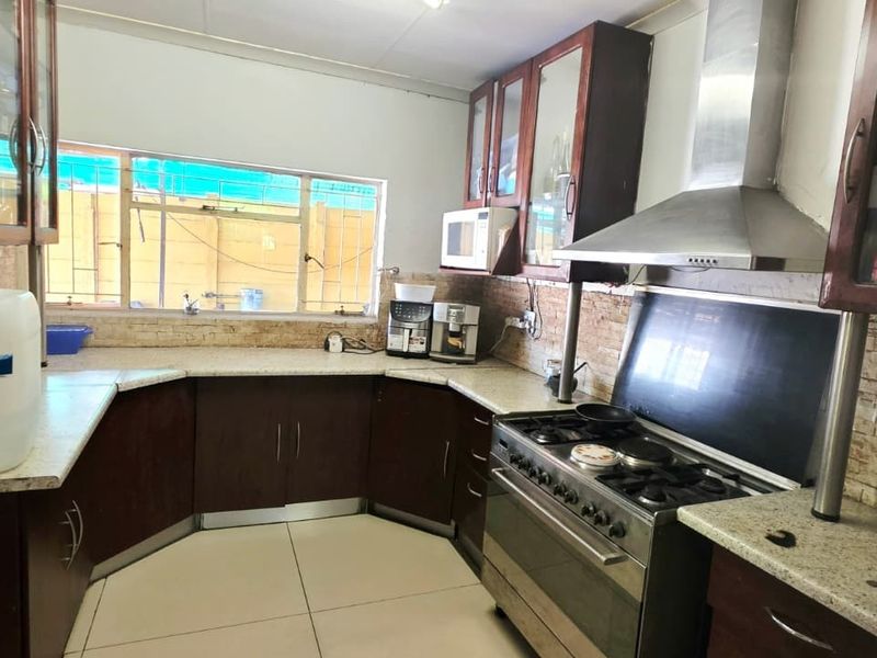A functional kitchen featuring dark wood cabinetry, granite countertops, a stainless steel gas stove with extractor fan, and a stone tile backsplash.