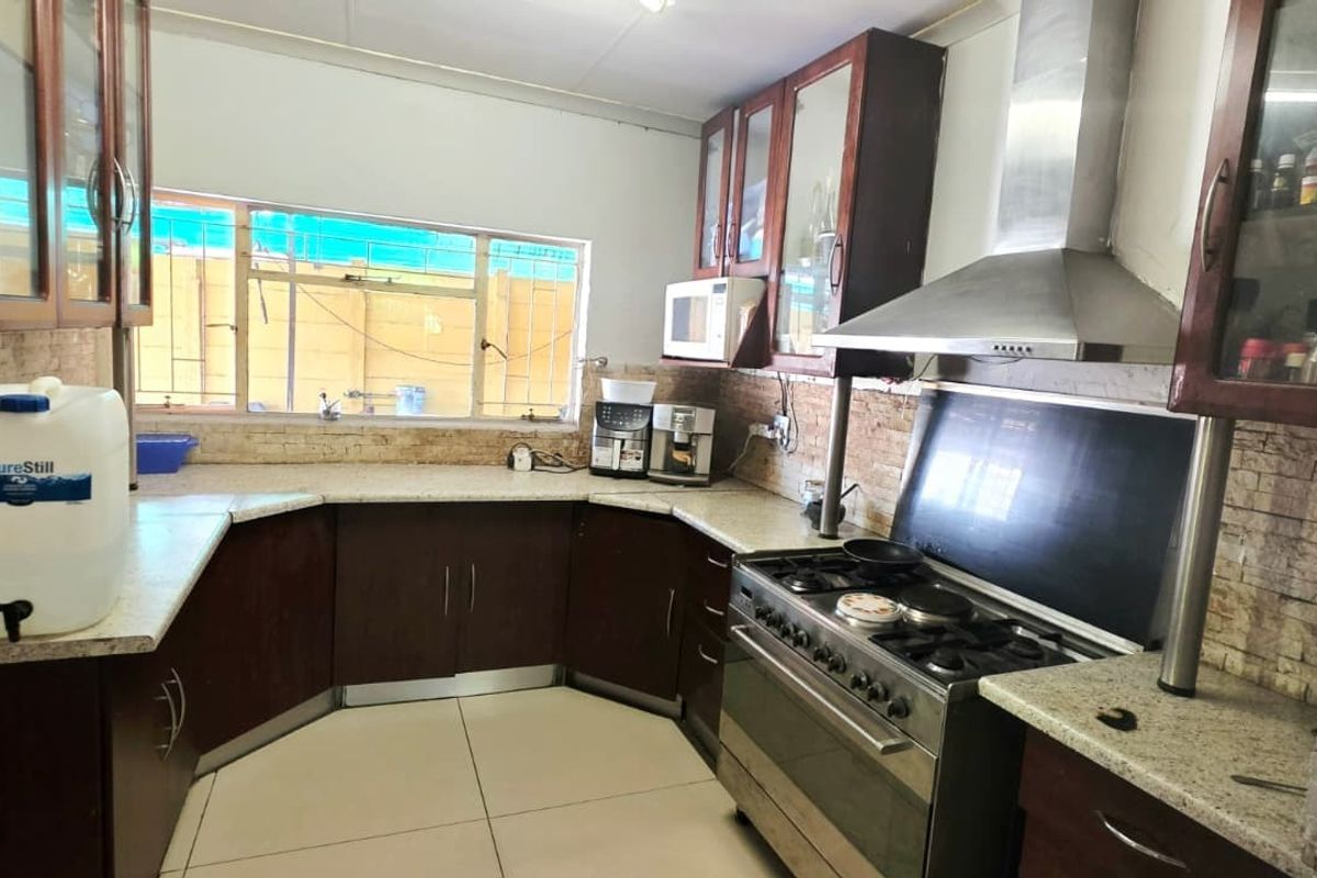 A functional kitchen featuring dark wood cabinetry, granite countertops, a stainless steel gas stove with extractor fan, and a stone tile backsplash.