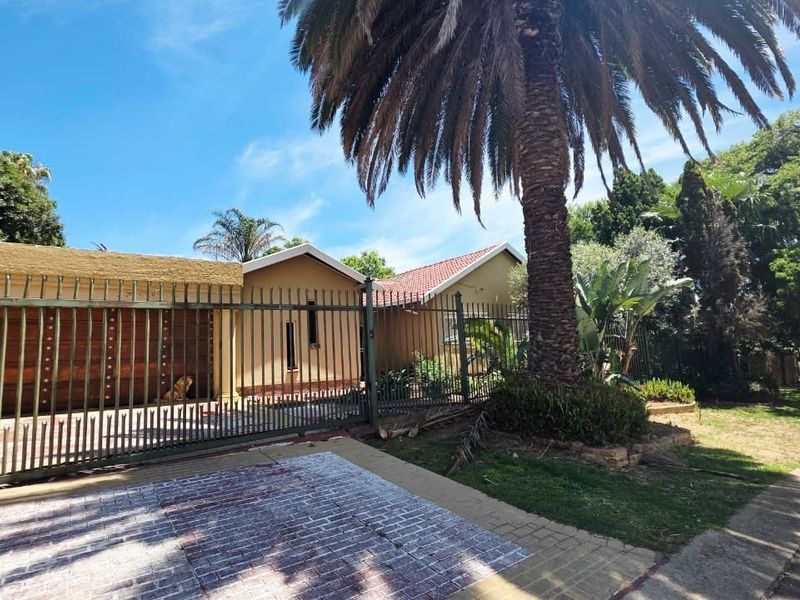 Front exterior view of the property featuring a gated driveway, tiled roof, and established garden with a large palm tree.