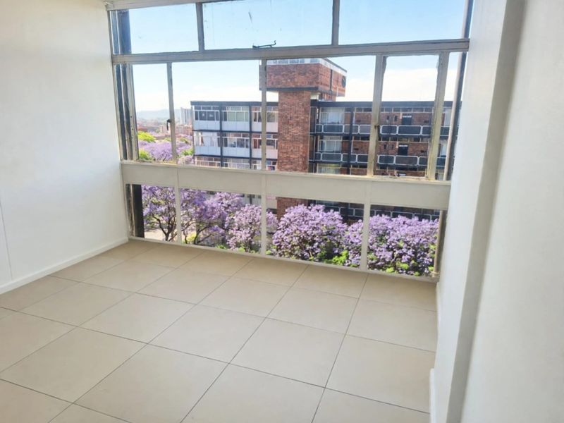 An enclosed balcony or sunroom featuring large windows with neighbourhood views and neutral tiled flooring, offering a bright and versatile additional living space.