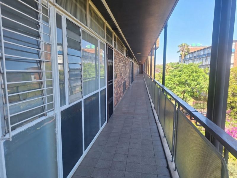A long, covered exterior balcony featuring tiled flooring, metal balustrades, and access to the apartment via louvre windows and a security gate.