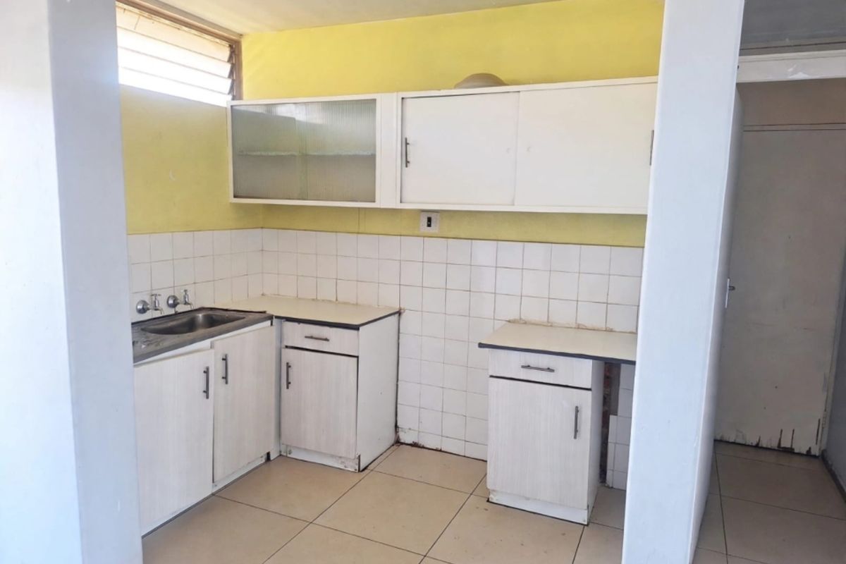 A dated kitchen featuring white built-in cabinetry, a stainless steel sink, tiled backsplash, and tiled flooring, offering significant potential for modernization.