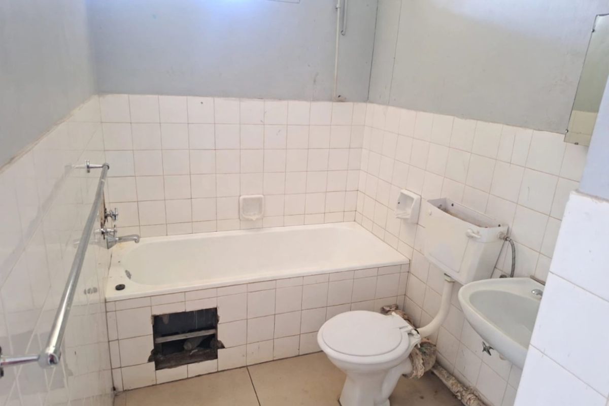 A dated bathroom featuring a standard bathtub, toilet, and washbasin with tiled finishes, currently requiring maintenance and cosmetic updates to improve its condition.