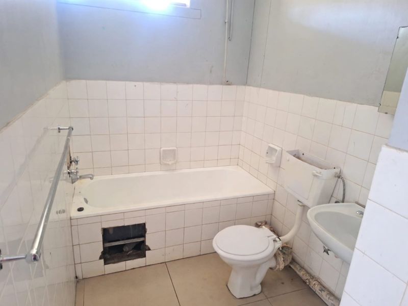 A dated bathroom featuring a standard bathtub, toilet, and washbasin with tiled finishes, currently requiring maintenance and cosmetic updates to improve its condition.