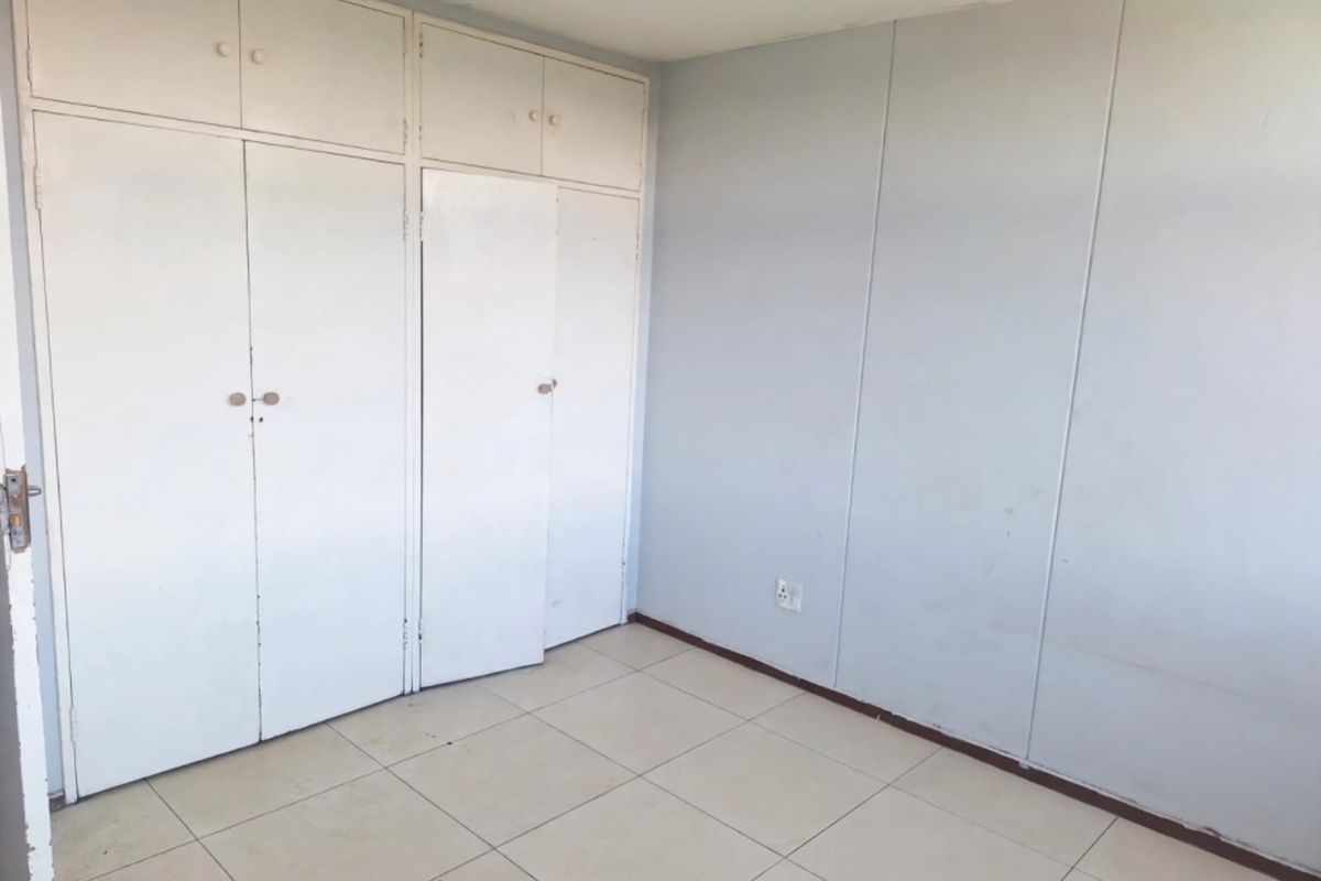 An empty bedroom featuring tiled flooring and built-in cupboards, offering a blank canvas for personalization.