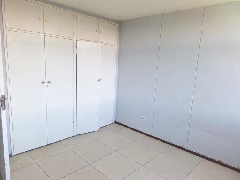 An empty bedroom featuring tiled flooring and built-in cupboards, offering a blank canvas for personalization.