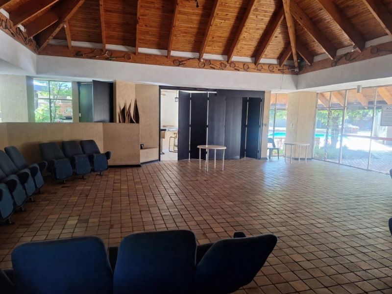 Spacious clubhouse area featuring a high exposed timber rafter ceiling, terracotta tile flooring, and large glass doors opening to the pool area.