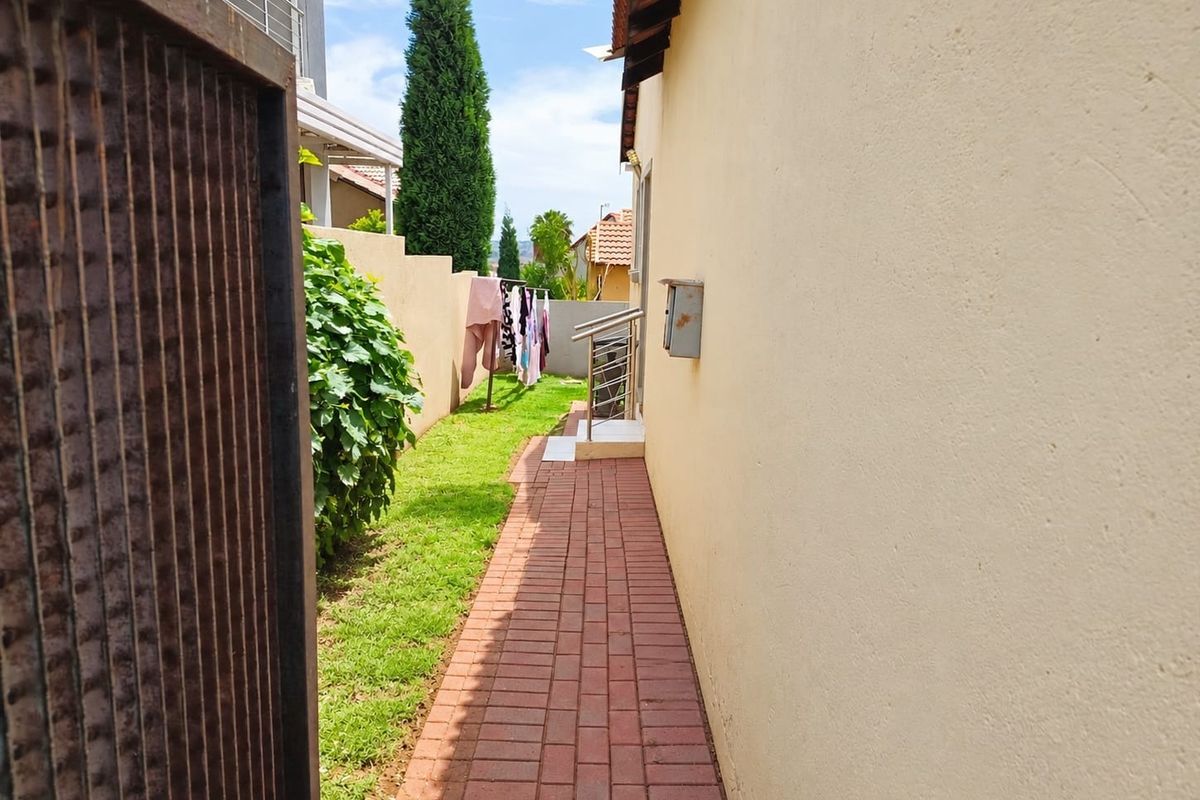 A side exterior walkway featuring brick paving, a boundary wall, and a metal handrail leading towards the rear garden area.