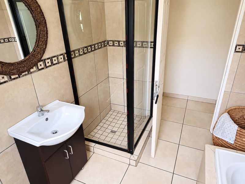 A functional bathroom featuring a corner shower enclosure, a vanity cabinet with a basin, and neutral wall and floor tiling.
