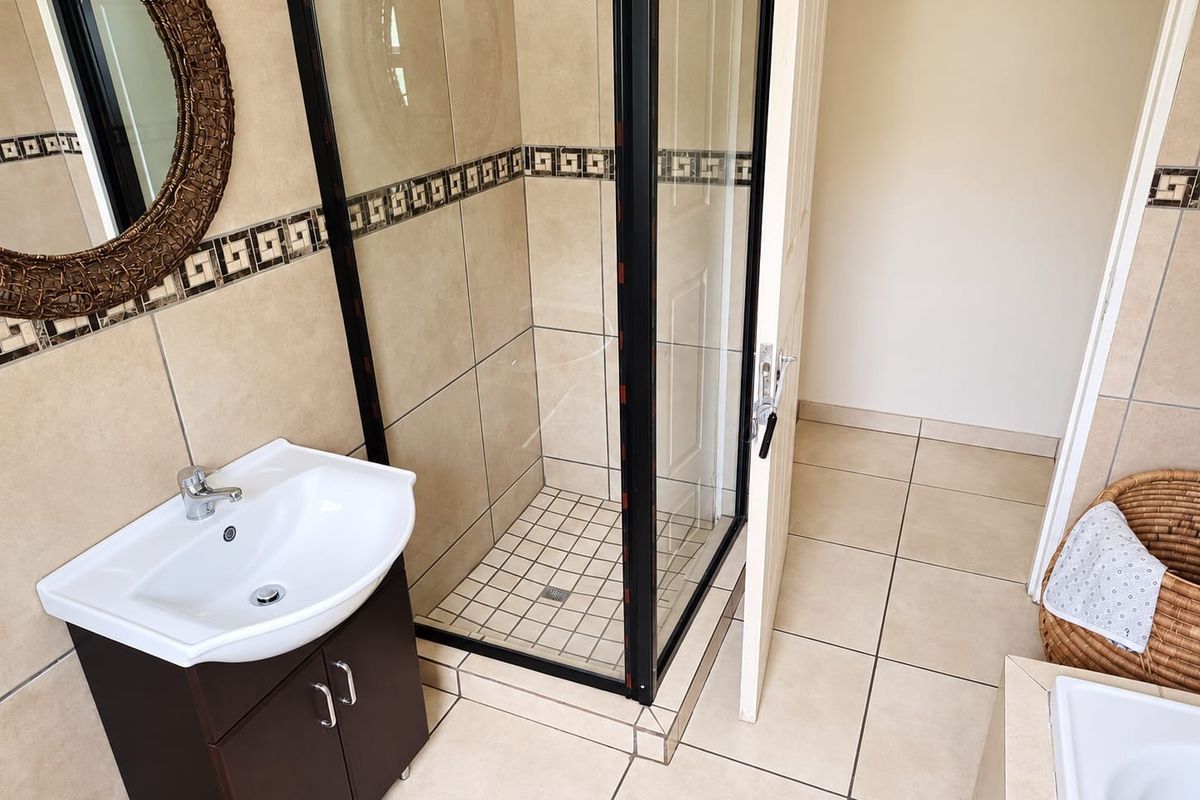 A functional bathroom featuring a corner shower enclosure, a vanity cabinet with a basin, and neutral wall and floor tiling.
