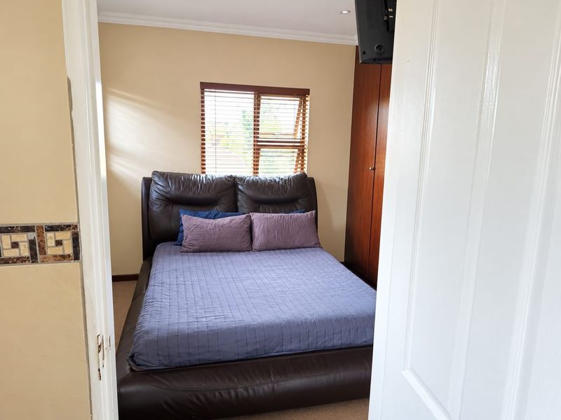 A functional bedroom featuring a built-in wooden wardrobe, venetian blinds, and recessed ceiling lighting.