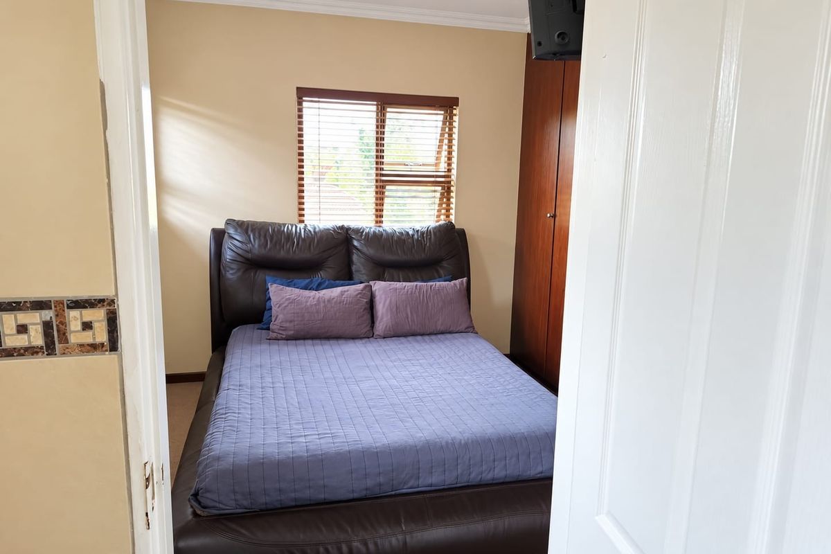 A functional bedroom featuring a built-in wooden wardrobe, venetian blinds, and recessed ceiling lighting.