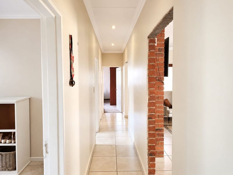 A bright hallway featuring tiled flooring, recessed downlighting, and an exposed brick feature wall leading to adjacent living spaces.
