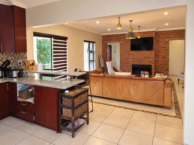 Spacious open-plan living area featuring a modern kitchen with granite countertops, a breakfast bar, and a cozy lounge with a brick fireplace.