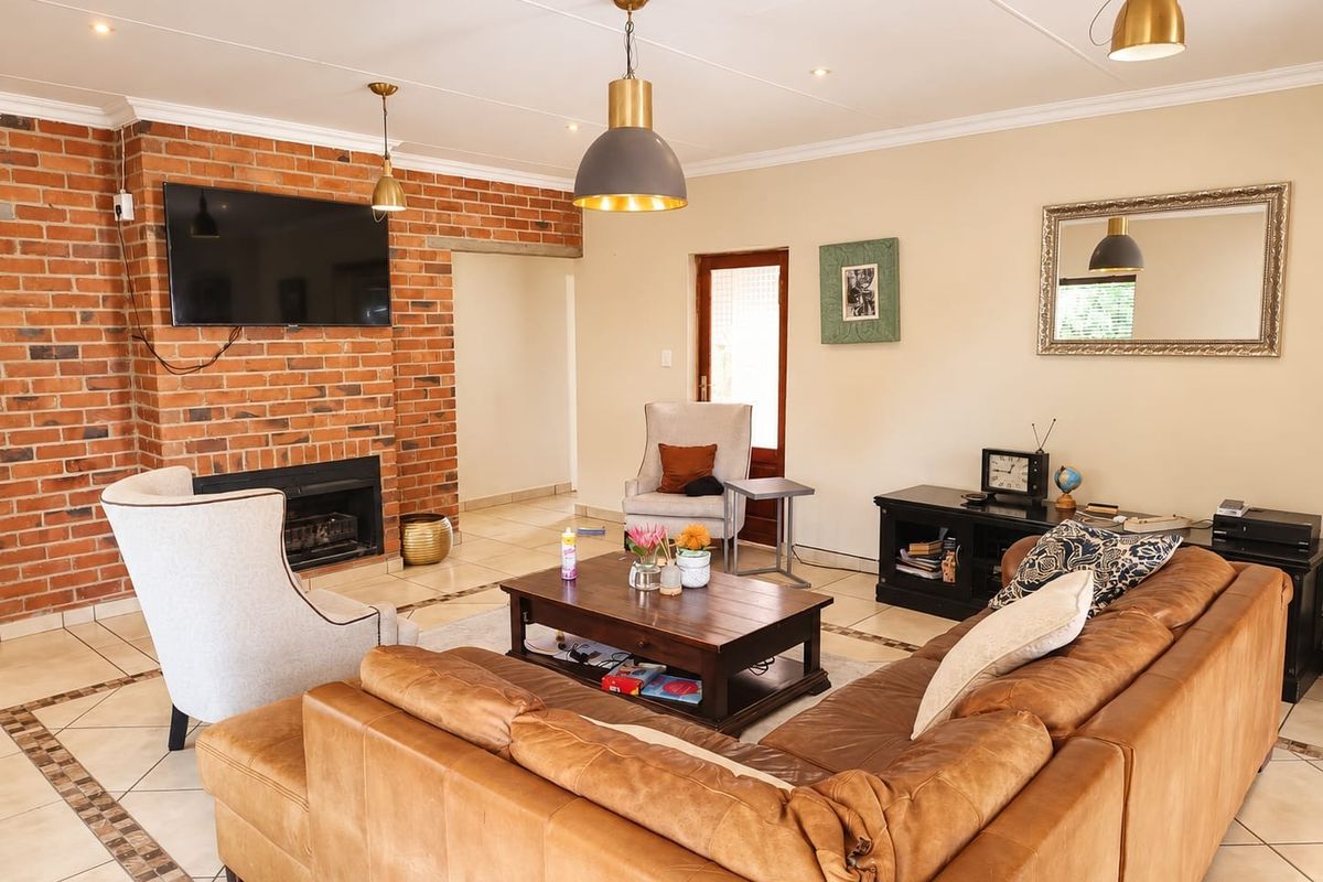 Spacious living room featuring an exposed brick fireplace, tiled flooring, and a combination of recessed and pendant lighting.