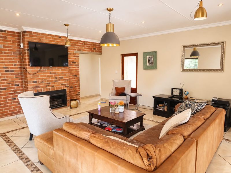 Spacious living room featuring an exposed brick fireplace, tiled flooring, and a combination of recessed and pendant lighting.
