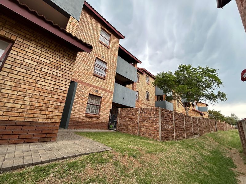 Exterior view of a multi-story apartment complex featuring face brick construction, paved walkways, and perimeter boundary walls.