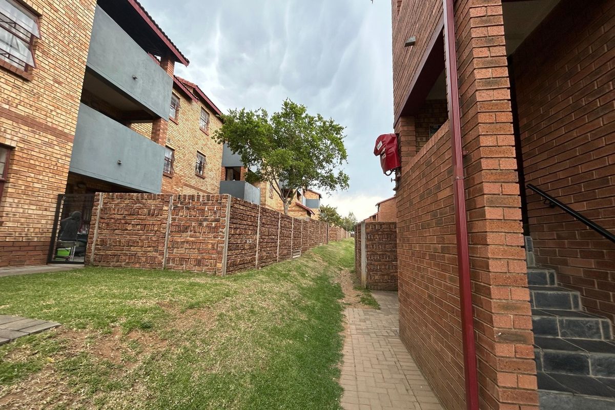 Exterior view of the apartment complex featuring face brick architecture, paved walkways, and communal garden areas between the residential blocks.