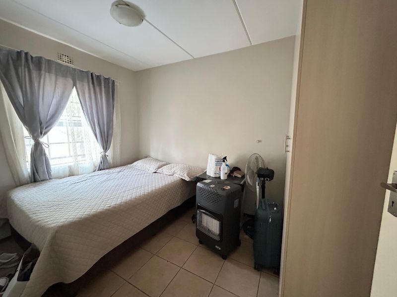 A functional bedroom featuring tiled flooring, a built-in cupboard, and a window fitted with security burglar bars.