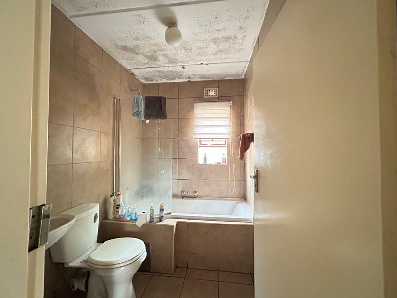 A dated bathroom featuring a built-in bathtub, shower screen, and pedestal basin, requiring ceiling repairs and general modernization of finishes.