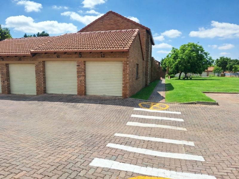 Exterior view of a brick apartment complex featuring multiple garage units, a paved driveway, and a well-maintained communal lawn area.