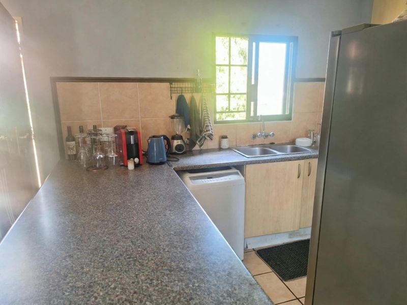 A functional kitchen featuring laminate countertops, a double basin sink, tiled backsplash, and built-in cabinetry with natural light from the window.