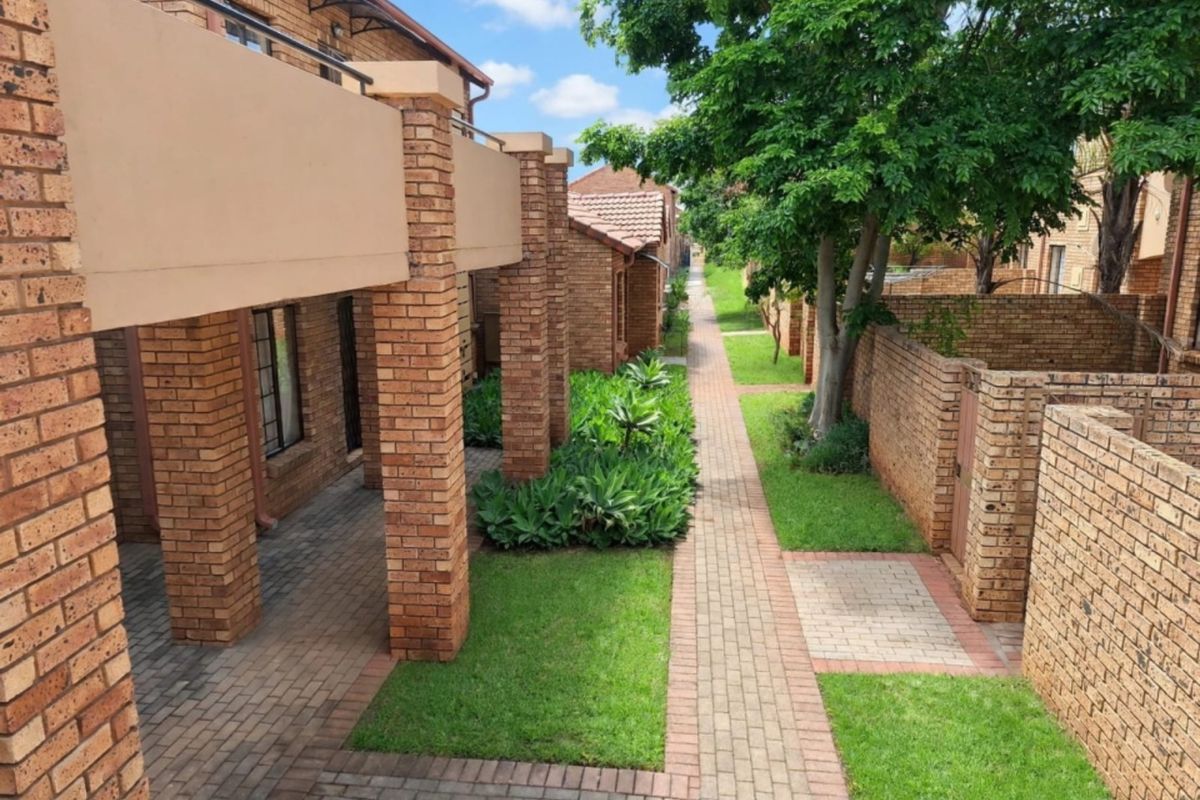 A well-maintained exterior view of the apartment complex featuring brick facades, covered patios, paved walkways, and established garden areas.